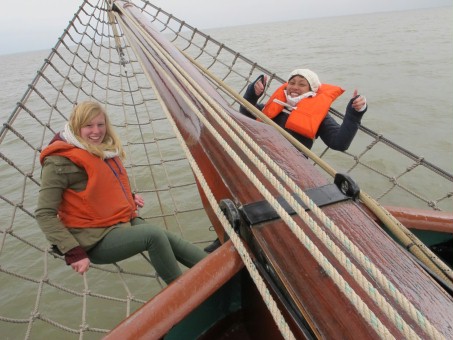 Zwei junge Freiwillige liegen im Klüvernetz auf einem Segelboot, während das Boot fährt.